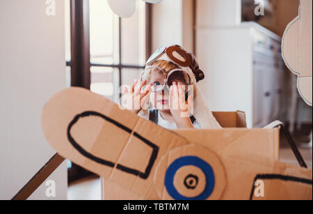 A toddler boy with carton plane playing indoors at home, flying concept.
