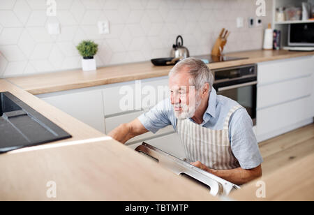 A senior man indoors in kitchen at home, loading dishwasher. Stock Photo