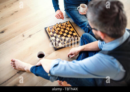 A midsection of adult son and senior father sitting on floor indoors, playing chess. Stock Photo