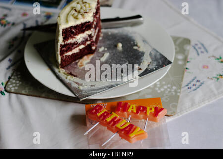 Colorful HAPPY BIRTHDAY greeting candles. Slice of red velvet cake on a white plate Stock Photo