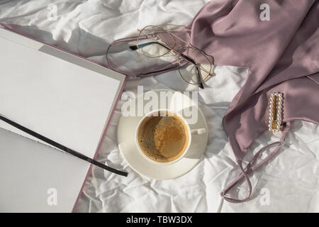 Feminine accessories, top and coffee on the white bed in the room full of natural sunlight Stock Photo