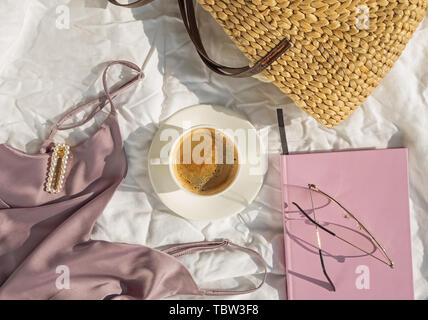 Feminine accessories, top and coffee on the white bed in the room full of natural sunlight Stock Photo