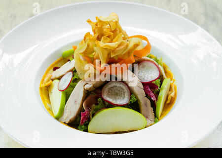 Close up of a fresh grilled chicken salad , Italian food recipe with radish, lettuce,fried topinambur gerusalem artichokes chips,sauce dressing on a w Stock Photo