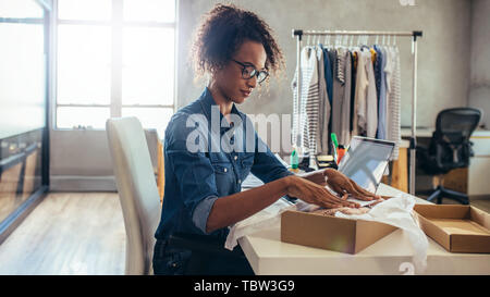 Woman online entrepreneur packing parcel box at office. Woman seller preparing product for delivery. Stock Photo