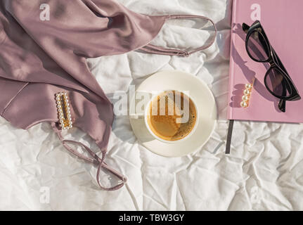 Feminine accessories, top and coffee on the white bed in the room full of natural sunlight Stock Photo