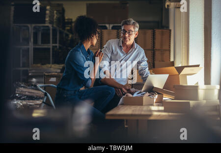 Two business partners working together at warehouse for online seller business. People discussing while preparing the package to delivery. Stock Photo