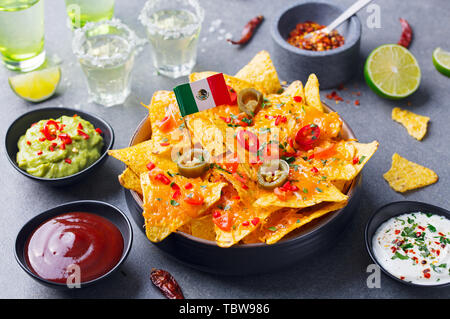 Nachos chips with Mexican flag and dips variety in black bowl. Grey stone background. Stock Photo