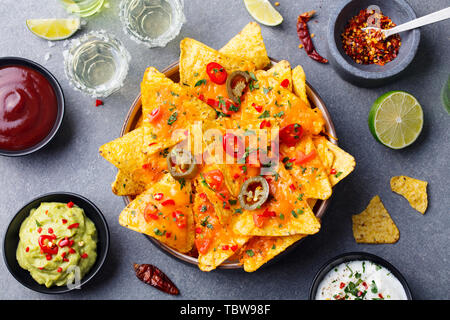 Nachos chips with melted cheese and dips variety in black bowl. Top view. Stock Photo