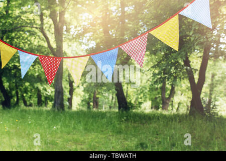 Colorful bunting flags hanging in park. Summer garden party. Outdoor birthday, wedding decoration. Midsummer, festa junina concept. Selective focus.,  Stock Photo