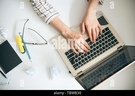 Top view of female hands working behind a laptop in a working office or home office. Or the student does the lessons or exercises. Stock Photo