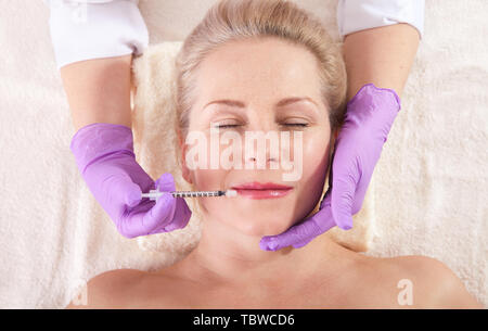 Middle aged woman gets cosmetic injection in her lips. Hyaluronic acid injection for facial rejuvenation procedure. Women in beauty salon. Plastic sur Stock Photo