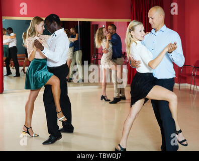 Adult dancing couples enjoying tango in dance studio Stock Photo