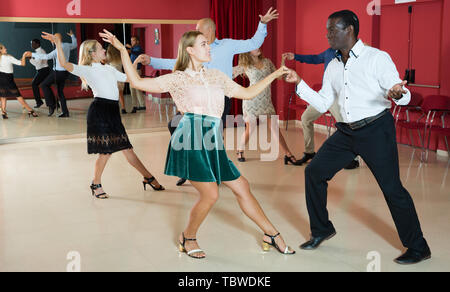 Young smiling people practicing vigorous jive movements in dance class Stock Photo
