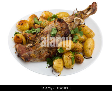 Baked lamb leg served with new potatoes and parsley Delicious baked lamb leg served with whole baked potatoes and garnished with parsley Appetizing la Stock Photo