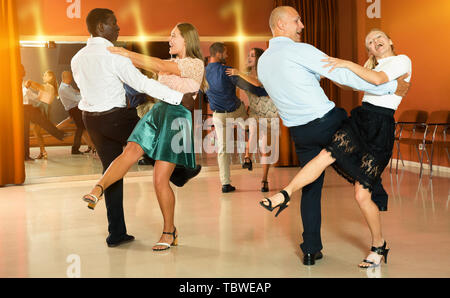 Young smiling people practicing vigorous jive movements in dance class Stock Photo