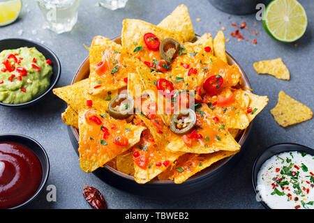Nachos chips with melted cheese and dips variety in black bowl. Grey stone background. Stock Photo