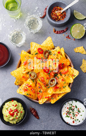 Nachos chips with melted cheese and dips variety in black bowl. Top view. Stock Photo