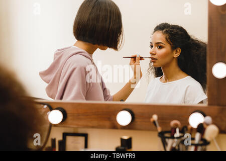 Professional make up artist applying pomade on a model in front of a mirror Stock Photo