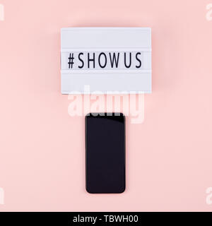 Creative top view flat lay of lightbox with hashtag Show Us message and mobile phone mockup pink background minimal style. Concept of Project world la Stock Photo