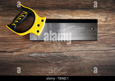 Handsaw with plastic yellow handle on vintage wooden table under dark dramatic moody lighting. Top down view. Stock Photo