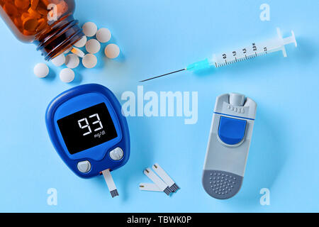 Diabetes monitoring and healthcare. Close up top down view of glucose meter, insulin pen, drug pills and syringe on blue background Stock Photo