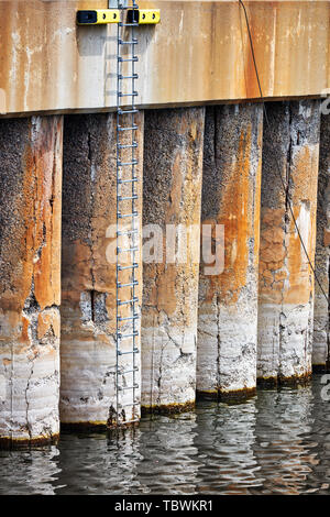 Metal climbing ladder mounted on the concrete columns of a harbor Stock Photo