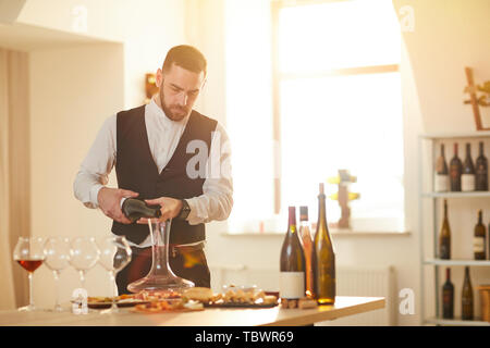 Portrait of professional sommelier pouring wine while preparing for wine tasting session in sunlight, copy space Stock Photo