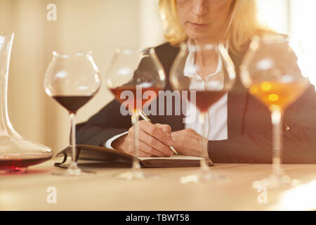 Mid-section portrait of female sommelier taking notes during tasting session with wine glasses in row, copy space Stock Photo