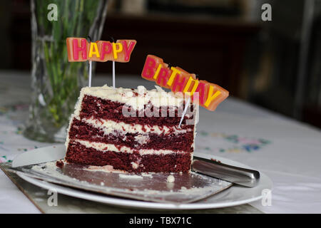 Colorful HAPPY BIRTHDAY greeting candles. Slice of red velvet cake on a white plate Stock Photo