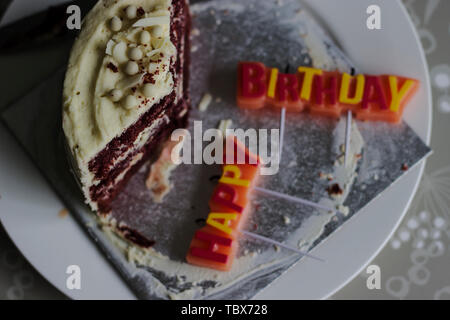 Colorful HAPPY BIRTHDAY greeting candles. Slice of red velvet cake on a white plate Stock Photo