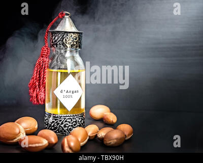 Decorative bottle with iron embossed in traditional Moroccan style with precious Moroccan argan oil and argan nuts on a dark black background with Stock Photo
