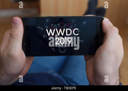 LOS ANGELES, CALIFORNIA - JUNE 3, 2019: Close up to male hands holding smartphone watching WWDC 2019. An illustrative editorial image. Stock Photo