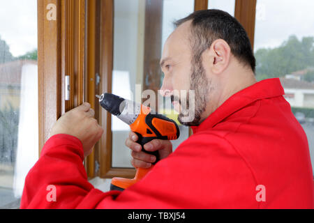 mature builder using drill on wooden windows Stock Photo