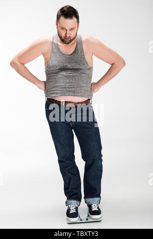 angry overweight man with hands akimbo standing on electronic weight scales and looking at camera isolated on white Stock Photo