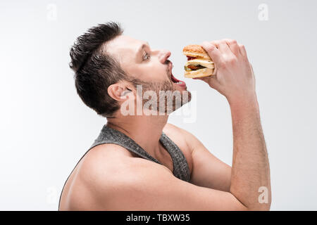 side view of chubby bearded man eating burger isolated on white Stock Photo