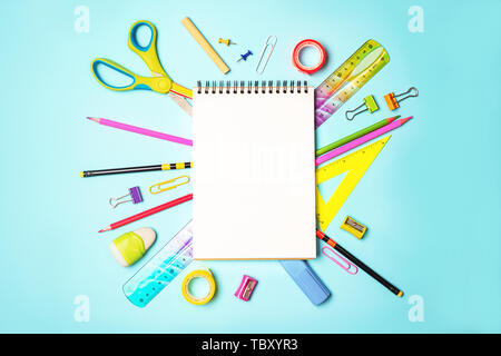 Back to school background with notepad, colorful pencils, square ruler, scissors, clips on pastel blue backdrop. Stock Photo