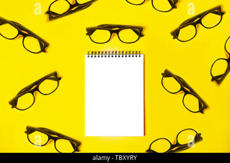 Notepad with trendy glasses on light yellow background. Stock Photo