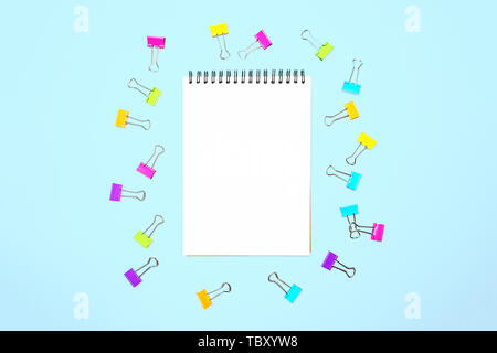 Back to school background with notepad, colorful paper clips on pastel blue backdrop. Stock Photo