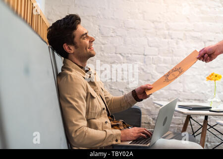 Smiling freelancer with laptop holding menu in cafe Stock Photo
