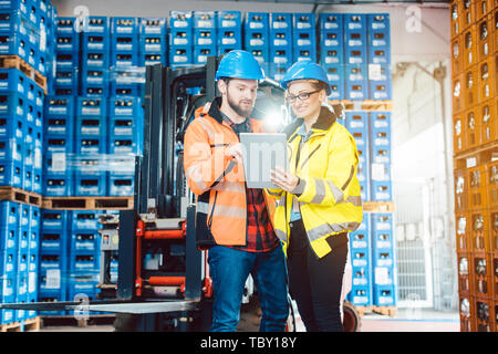Workers in warehouse checking data on tablet computer with forklift in the background Stock Photo
