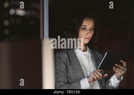 Focused businesswoman using her tablet in a dark office Stock Photo