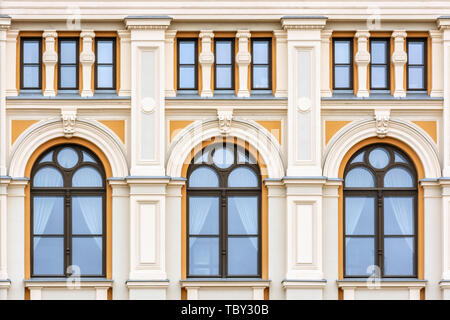 Windows with an arch on the facade of the orange wall of a residential building with columns in the old part of Riga city. From the window series of t Stock Photo