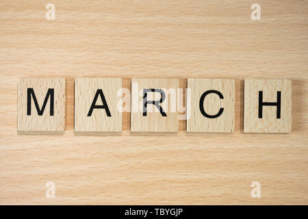 The word March, spelt out using wooden tiles on a wood effect background. Stock Photo