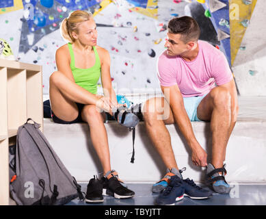 Smiling positive pair of sports people dressing for mountaineering outfit for climbing on artificial rock wall indoors Stock Photo