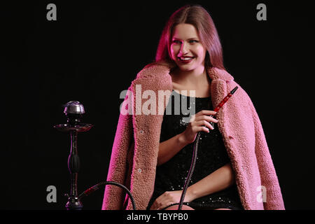 Young woman smoking hookah on dark background Stock Photo