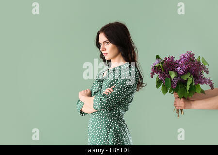 Offended young woman refusing to take bouquet of lilac flowers on color background Stock Photo