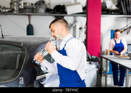 Concentrated mechanic performing car body repair at auto workshop with tools for repairing dents Stock Photo