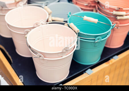 Various multicolored bright small ornamental metal buckets for sale on wooden table outdoors. Many colorful decorative mini pails for garden flower Stock Photo