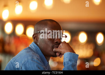 Warm toned portrait of pensive African-American man sitting at table window in cafe Stock Photo