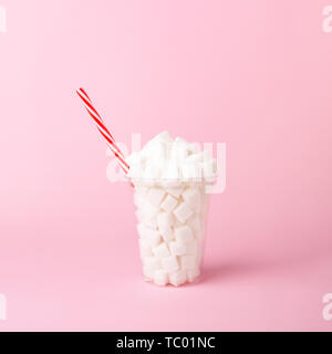 Plastic shake glass with straw full of sugar cubes on pastel pink background. Unhealthy drink concept. Minimal, vertical, side view. Stock Photo